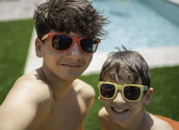 Renkli güneş gözlüğü takan iki mutlu kardeş yaz tatilinde havuz kenarında selfie çekiyorlar.
