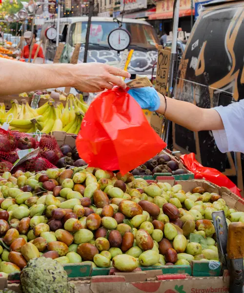 Çinli satıcı mavi eldiven giyerek Çin Mahallesi, New York 'taki açık hava pazarında müşteriye kırmızı jübile uzatıyor. 5 Eylül 2024.
