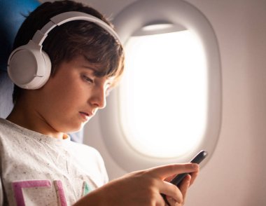 Akıllı telefon kullanan ve kulaklıkla müzik dinleyen genç bir çocuğun portresi.