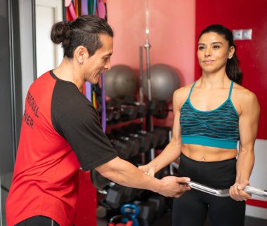 Modern bir spor salonunda halter egzersizi yaparken sportif bir kadına yardımcı olan İspanyol kişisel antrenör. Fitness ve sağlıklı yaşam tarzı konsepti