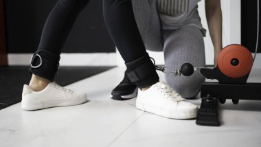 Sporcu kadın spor salonuna hazırlanıyor. Spor salonundaki kablo makinesine ayak bileği ağırlığı takıyor.