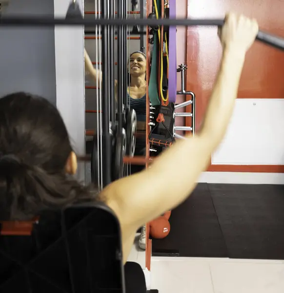 Spor salonundaki spor aletlerini kullanarak sırt kaslarını çalıştıran spor kadınlarına yakın çekim.