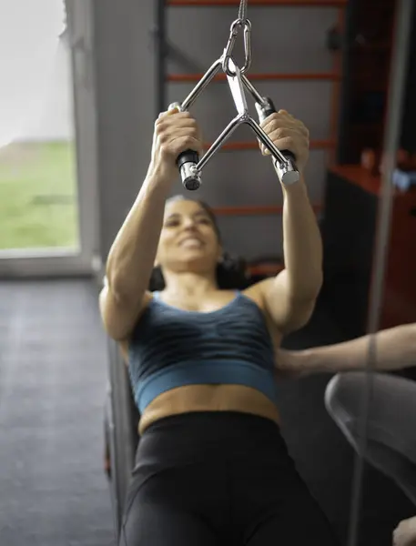 Kadın kişisel antrenörünün yardımıyla kablo sırası makinesi kullanarak sırt kaslarını çalıştırıyor