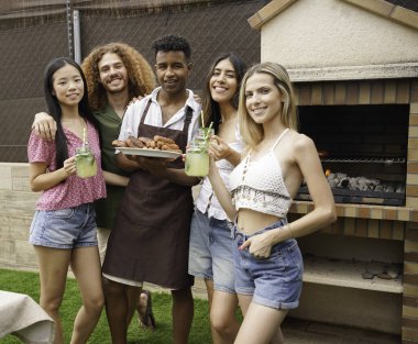 Neşeli genç arkadaşlar ferahlatıcı içeceklerin ve lezzetli barbekü yemeklerinin tadını çıkarıyorlar. Yazı arka bahçede kutluyorlar.