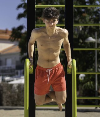 Açık havada egzersiz yapan bir gencin portresi, vücudunun üst kısmını jimnastik yaparken paralel çubuklar kullanarak güçlendirmek.