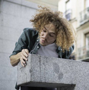 Kıvırcık saçlı adam şehirdeki taştan bir çeşmeden tatlı su içiyor.
