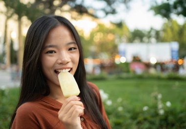 Genç Asyalı bir kadının yaz parkında fotokopi çekilen bir çubukta dondurmanın tadını çıkarırken fotoğrafı.,