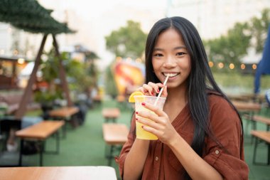 Gülümseyen genç bir kadın açık hava gıda pazarında ferahlatıcı bir içecek içiyor ya da fotokopi alanı olan bir bira bahçesi