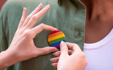 Kadın ellerine bir gökkuşağı lgbtq onur rozeti takılıyor. Bu rozet gurur ayının kutlanmasını ve desteğini simgeliyor.