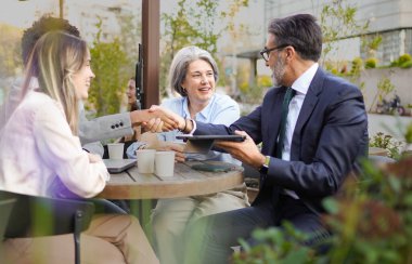 İş ortakları açık bir kafede anlaşma yaptıktan sonra el sıkışıyor ve başarılı anlaşmalarını kutluyorlar.