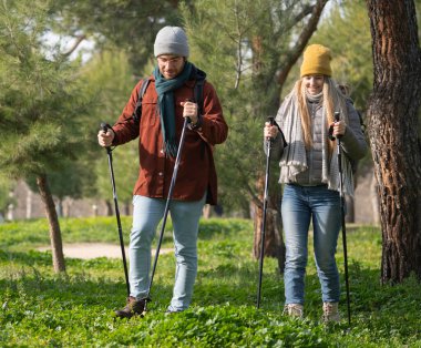 Genç çift doğa yürüyüşünün tadını çıkarıyor, destek için sırıkları kullanıyorlar. Sağlıklı yaşam tarzı kavramı