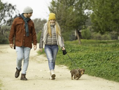 Gülümseyen genç bir çift parkta köpeklerini gezdiriyorlar. Kış günü fotokopi çektikleri yerde rahatça geziniyorlar.