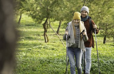 Mutlu genç çift doğa yürüyüşünün tadını çıkarıyor, yürüyüş direkleri kullanıyor ve fotokopi çekilen kışlık giysiler giyiyorlar..
