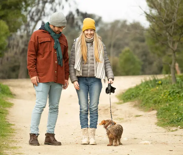 Genç çift, kıtır bir kış gününde tüylü dachshund köpeğiyle sakin bir gezintinin tadını çıkarıyor.