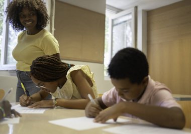 Mutlu Afrikalı öğretmen öğrencilerin masalarda derslerine konsantre olmalarını izliyor.