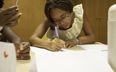 Afro genç siyahi bir öğrenci bir sınıf ortamında ders sırasında yazmaya odaklanıyor.