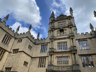 Oxford Üniversitesi 'nin görkemli Gotik mimarisi mavi gökyüzüne karşı. Karmaşık kuleler, geniş pencereler ve dekoratif unsurlarla süslü taş cephe. Iconic İngiliz akademik simgesi.