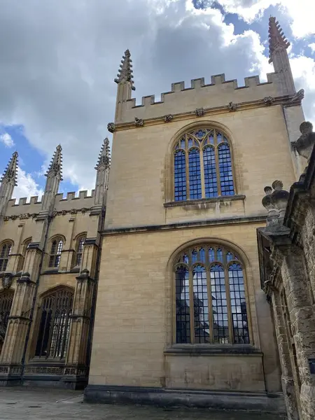 Bal rengi kireç taşı duvarlar, sivri kemerler, süslü çıkıntılar ve geniş pencereli tarihi Oxford Üniversitesi binasının gotik mimari detayları..