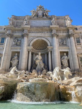 Roma 'daki Iconic Trevi Çeşmesi parlak mavi gökyüzüne karşı. Barok başyapıtında süslü taş heykeller, çağlayan su ve ayrıntılı mimari ayrıntılar yer alıyor. Mitolojik figürleri olan ünlü İtalyan simgesi.