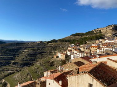 Beyaz boyalı ve terasotta çatıları olan taştan binaları olan İspanyol dağ köyü. Uçsuz bucaksız manzaralı kayalık yamaçlara ve parlak mavi gökyüzünün altındaki uzak dağlara yuva yapmış..