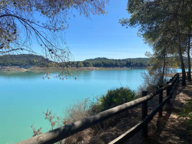 Dağlarda bir göl. Tahta çitlerle çevrili yürüyüş parkurundan görülen sakin turkuaz göl. Açık mavi gökyüzü, sakin suları çevreleyen zümrüt ormanlarıyla çelişiyor.. 