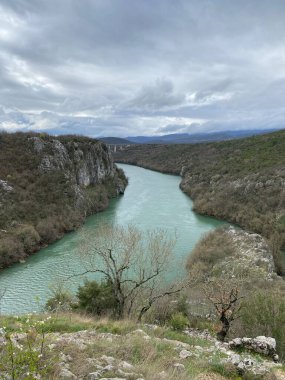 Cetina Nehri 'nin turkuaz suları Hırvatistan' daki dramatik kayalık kanyondan geçiyor. Bulutlu gökyüzü sarp kayalıkların ve seyrek bitki örtüsünün üzerinde dengesiz bir atmosfer yaratır..