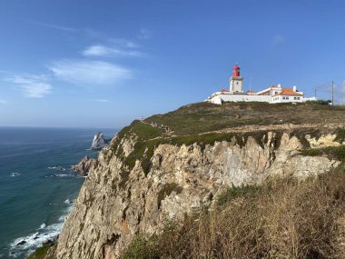 Cabo da Roca deniz feneri dramatik kireçtaşı uçurumlarına tünemişti. Portekiz 'in en batı noktası Atlantik Okyanusu' na bakıyor. Gökyüzüne karşı beyaz binaların arasında kırmızı tepeli işaret feneri duruyor..