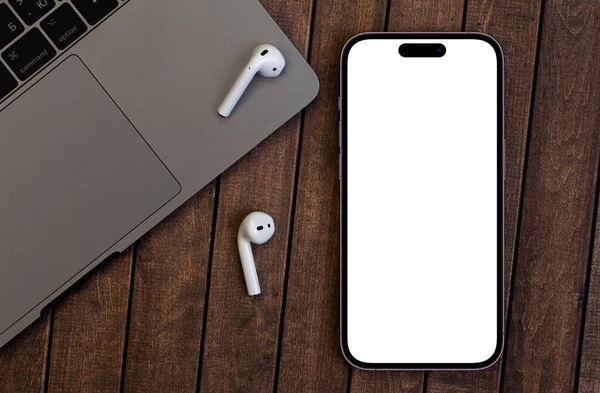 木製の背景にAirpods付きの白い画面とMacbookでモックアップスマートフォンのIphone Pro Max Appleは多国籍テクノロジー企業です ジョージア州バトゥミ 2022年10月26日 — ストック写真