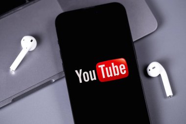 Youtube mobil logo uygulaması AirPods kulaklıklı akıllı telefon iPhone ekranında. YouTube herkesin izleyebileceği ücretsiz bir video paylaşım uygulamasıdır. Batum, Gürcistan - 5 Kasım 2023