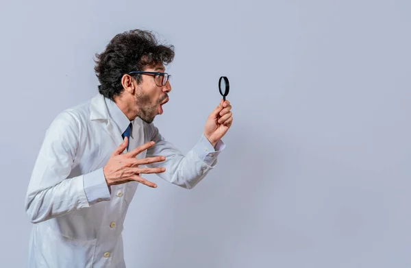 Scientist holding a magnifying glass looking to the side, Man in a white coat with a magnifying glass looking advertisement, Surprised scientist observing with a magnifying glass to the side