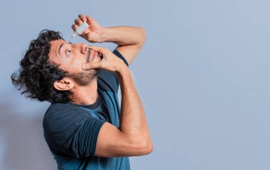 Sinirli gözlere ferahlatıcı damlalar süren insanlar. Gözüne damlatıcı koyan adam izole edilmiş. Gözü tahriş olmuş bir adam, bir damlacıkla damlalar uyguluyor, bir kişi, tahriş olmuş göz damlasına damlatıcı uyguluyor.