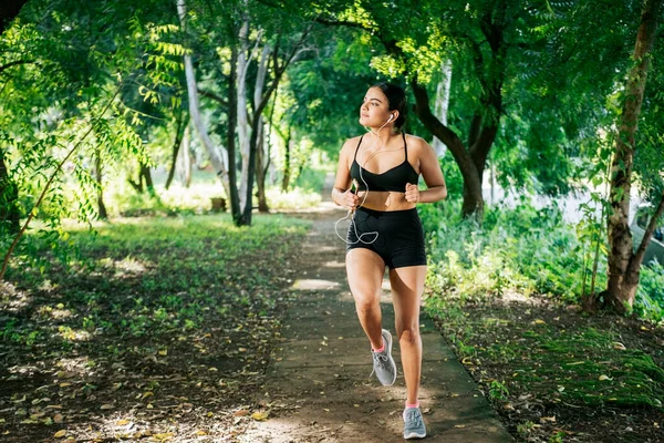 stock image Sporty young woman running in a park. A girl running in a park while listening to music. Lifestyle of beautiful girl running in a park surrounded by trees. Healthy lifestyle concept