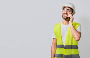Telefondaki gülümseyen mühendis kopyalama alanı ile izole edilmiş konuşuyor. Çelik yelek giyen genç mühendis cep telefonuyla konuşuyor. İnşaat mühendisi kavramı cep telefonundan konuşuluyor.