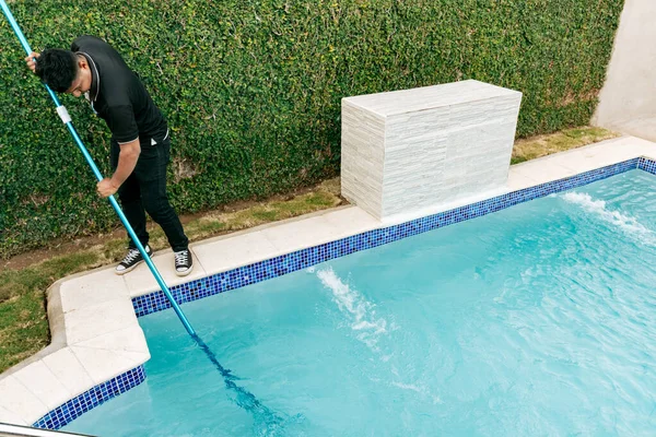 Maintenance person cleaning a swimming pool with skimmer, Worker cleaning a pool with skimmer. Swimming pool cleaning and maintenance concept