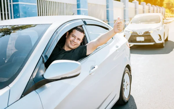 Smiling driver giving a thumbs up on the road. Satisfied driver man showing thumb up, safe driving concept. Young driver man in the car showing thumb up
