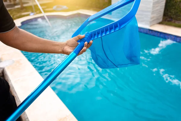 Person with skimmer cleaning pool, Hands holding a skimmer with blue pool in the background. Man cleaning the pool with the Skimmer, A man cleaning pool with leaf skimmer