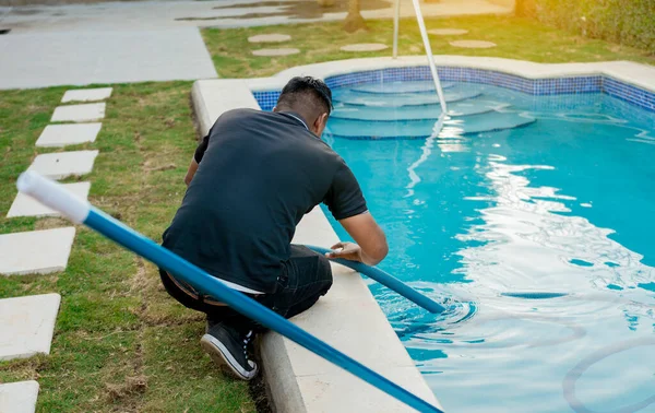 Maintenance person cleaning swimming pool with suction hose. Cleaning and maintenance of swimming pools with suction hose. Crouched man cleaning swimming pool with vacuum hose