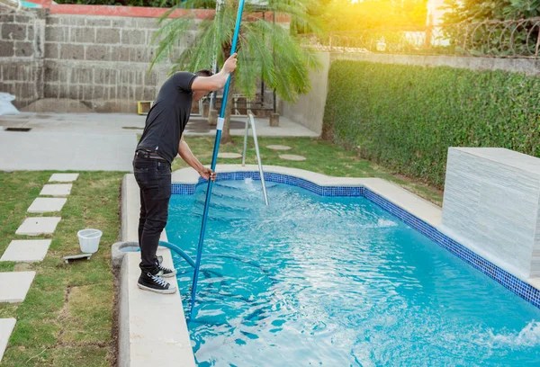 Man cleaning and maintaining swimming pools with a suction hose. Young man cleaning a swimming pool with a vacuum hose, Maintenance person cleaning pool with vacuum hose