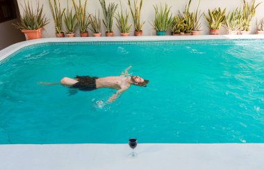 Man on vacation swimming on his back in a swimming pool. Young man swimming on his back in a hotel pool. Concept of man on vacation enjoying the pool