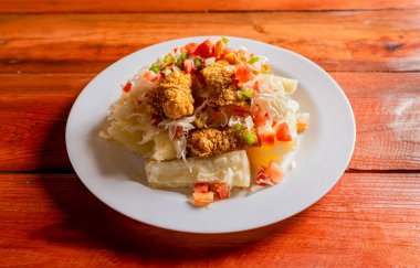 Cassava ve domates salatalı geleneksel chicharron yemeği. Latin yemekleri chicharron con yuca ahşap masada servis edilir. Nikaragua usulü Chicharron tabağı. Masada manyok var..