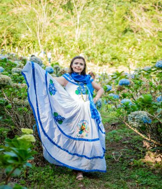 Çiçeklerle çevrili bir tarlada ulusal halk kostümü içinde gülümseyen kadın. Nikaragua 'da halk kostümü giyen insanlar. Geleneksel folklor kostümlü Nikaragualı kadın Milflores tarlasında