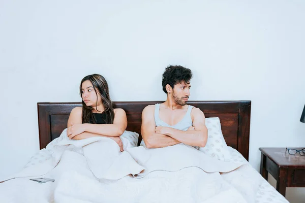 Conflicting couple sitting on bed, Upset couple sitting on bed with crossed arms. Young couple arguing sitting in bed, Upset couple sitting on the bed