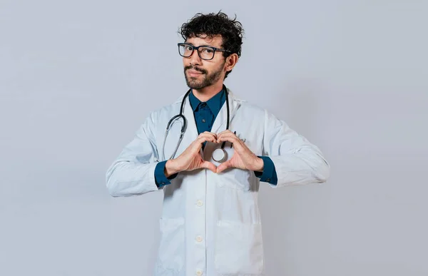 英俊的医生用手做心脏动作 快乐的医生指指点点 年轻医生使心脏形同孤立 — 图库照片