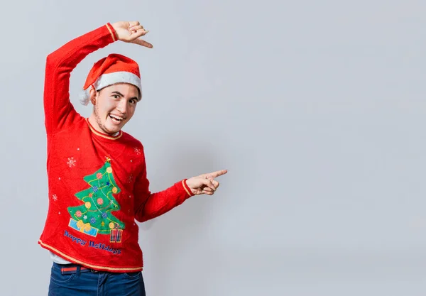 Friendly Christmas man pointing to a space to the side. Friendly smiling young man in christmas clothes pointing at a promo, Cheerful christmas man concept pointing promo offer isolated