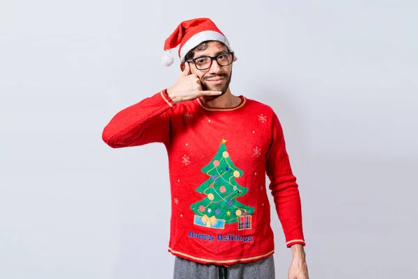 People in Christmas clothes making a call gesture with their fingers. Man in christmas hat imitating a phone conversation, Young latin man in christmas hat making a call gesture isolated