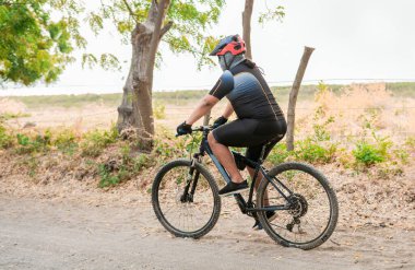 Tombul bisikletçi yolda. Toprak yolda profesyonel bisikletçi, ağaçlarla çevrili toprak yolda şişman bisikletçi.