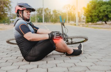 Diz ağrısı olan bir bisikletçi. Erkek bisikletçi diz ağrısıyla kaldırımda oturuyor. Dışarıda dizinden sakatlanan bir bisikletçi kavramı.