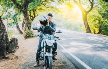 Güvenlik kaskı takan motosikletli adama yakın çekim. Motosiklet asfalt yolunun yanında kaskını takıyor. Motosiklet güvenliği kavramı