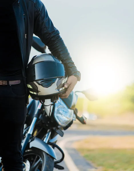 摩托车安全帽的概念 无法辨认的自行车手在公路附近的摩托车旁边拿着头盔 骑摩托车的人戴着安全帽 紧挨着路边的摩托车 — 图库照片