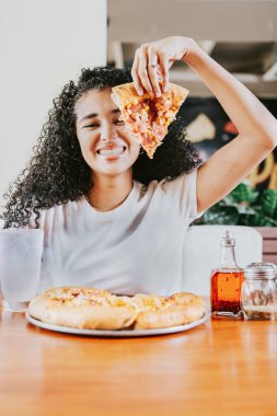 Bir restoranda pizza yerken gülümseyen afro kadın. Lokantada pizza gösteren mutlu afro saçlı kadın.